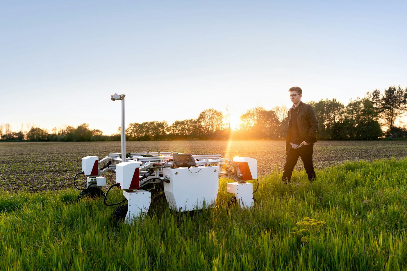 Engineer walking beside an autonomous field robot at sunset