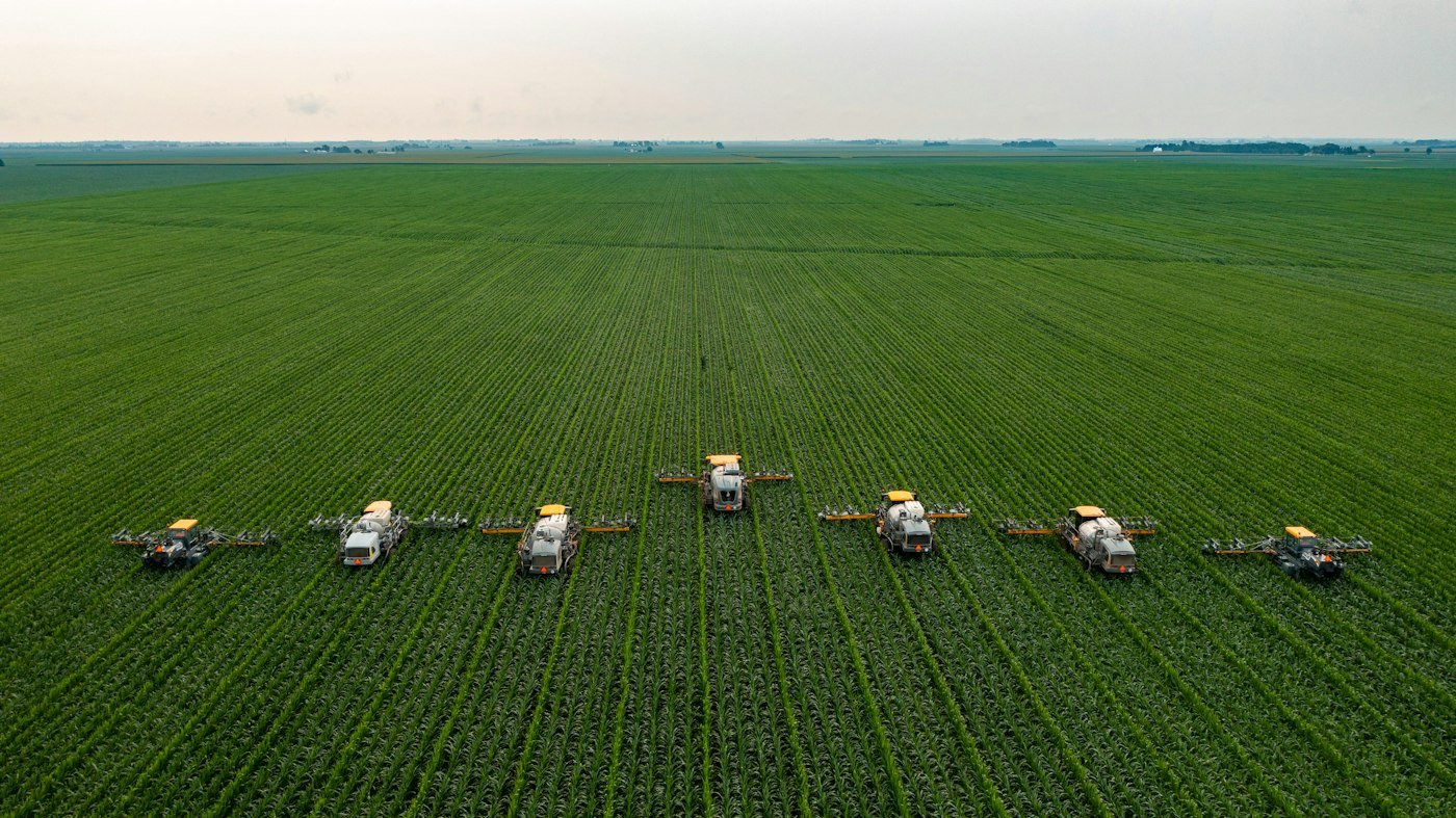Aerial view of agricultural sprayers moving through a green corn field